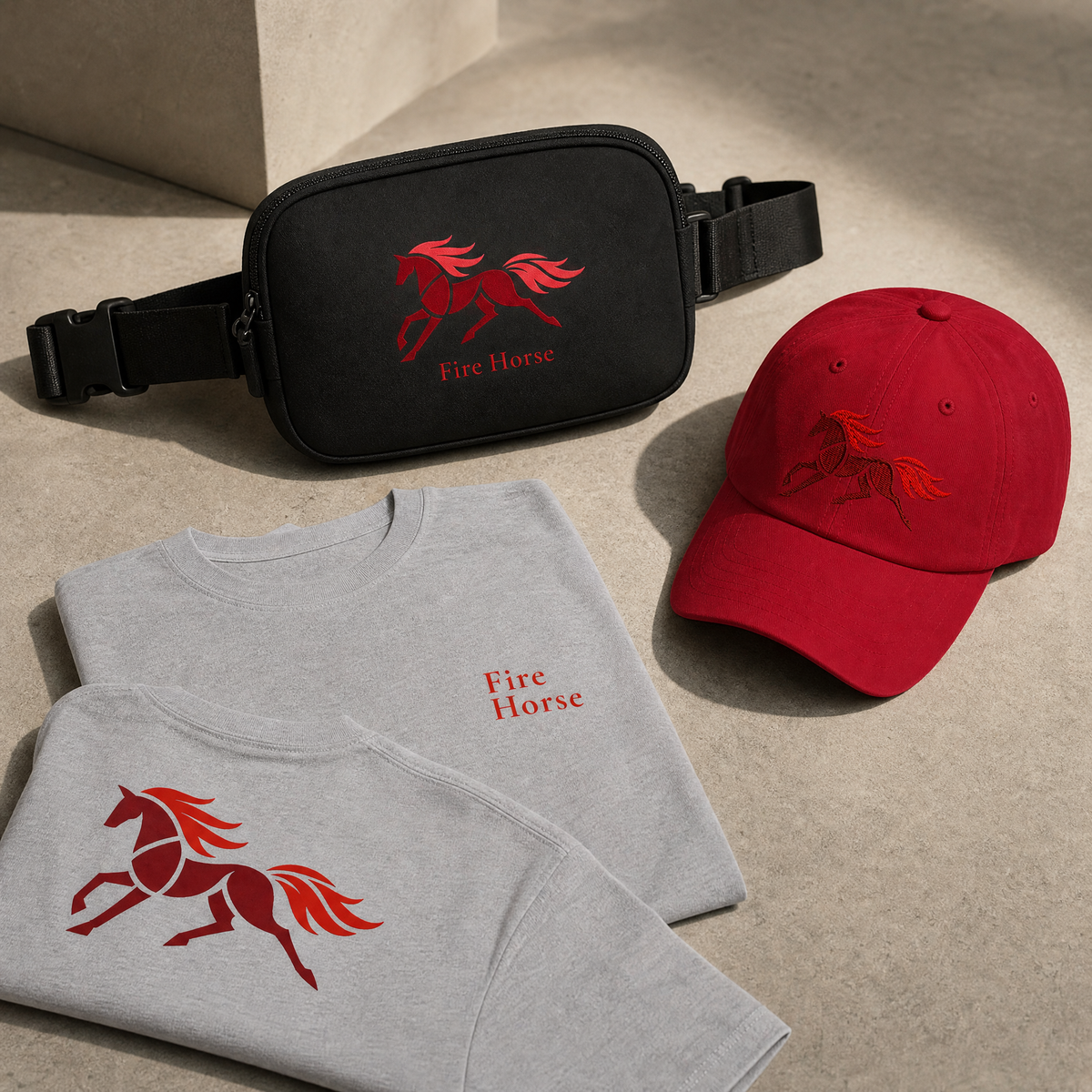 A coordinated Fire Horse graphic merchandise set arranged on a light stone surface, including a black crossbody bag, a folded light gray T-shirt, a red baseball cap, and a matching red embroidered horse logo on the shirt and cap.