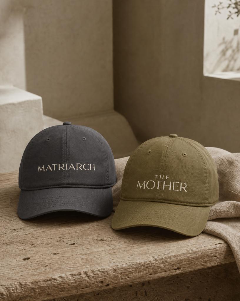 Charcoal MATRIARCH embroidered cap and olive THE MOTHER embroidered cap from the Atlas Stitch Mother Capsule on a warm neutral background.
